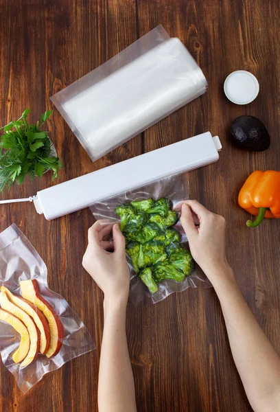 The process of packing pieces of fresh broccoli in a vacuum bag and sealing with a vacuum cleaner on a wooden dark table. Copy space text