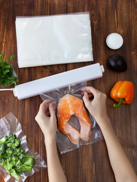 The process of packing a piece of fresh red fish into a vacuum bag and sealing with a vacuum cleaner on a wooden dark table. Copy space text