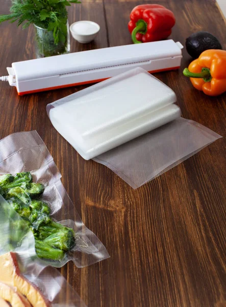 A roll of empty small vacuum bags next to a vacuum cleaner and packed pieces of fresh broccoli in a vacuum bag on a wooden dark table. Copy space text