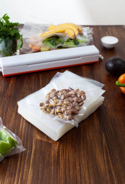 A pack of empty vacuum bags and packed vacuum nuts with vegetables on a dark wooden table. Copy space text