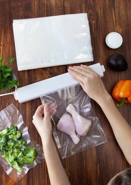 The process of packing raw chicken legs in a vacuum bag and sealing with a vacuum cleaner on a wooden dark table. Copy space text