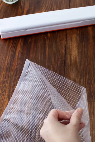 A woman\'s hand opens a vacuum bag for packing products with a vacuum cleaner at home on a dark wooden table. Copy space text