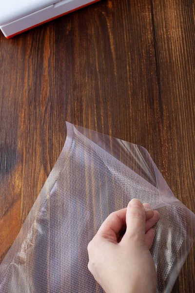 Top view of an empty vacuum bag in a woman\'s hand on a dark wooden table. Large. Copy space text