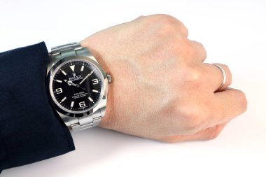 Rolex klasik kol saati siyah istiridye daimi kâşif 1 modeli masanın beyaz arka planına sahip başarılı bir iş adamının sol bileğinde. 
