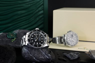 Rolex klasik kol saati seramik model siyah istiridye daimi denizaltı tarihi 40 mm siyah masa üzerinde küçük taşlar ve yeşil kutu arkaplan