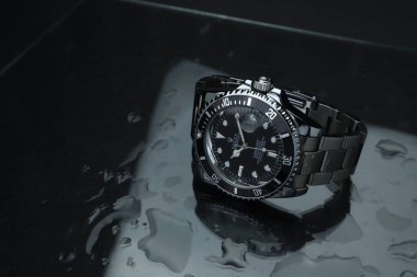 Rolex klasik kol saati seramik model siyah istiridye daimi denizaltı tarihi 39 mm karanlık odadaki ıslak siyah masada ve karanlık arka planda.