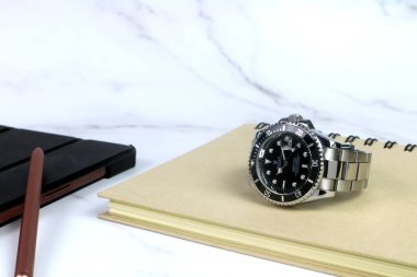 Rolex klasik kol saati seramik bezel modeli siyah istiridye daimi denizaltı tarihi 39 mm beyaz mermer masa üzerinde bir defter ile