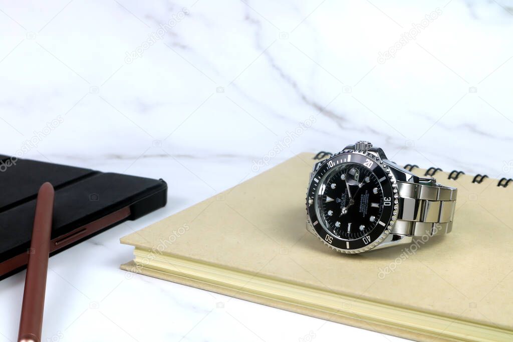 The Rolex vintage wristwatch ceramic bezel model black oyster perpetual submariner date 39 mm display on white marble table with a notebook