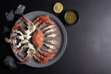 Yuvarlak tabakta kaynamış mavi yüzme yengeci, deniz ürünleri restoranında akşam yemeği sırasında limon ve taşlarla birlikte ahşap siyah masanın üzerinde.