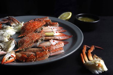 Yuvarlak tabakta kaynamış mavi yüzme yengeci Hong Kong 'daki deniz ürünleri restoranında akşam yemeği sırasında limonla birlikte ahşap siyah masada.