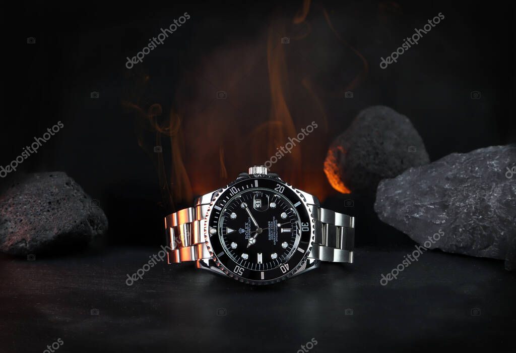 The Rolex vintage wristwatch ceramic bezel model black oyster perpetual submariner date 39 mm display on black table with background of flame and rocks in the dark shelf of luxury watch exhibition