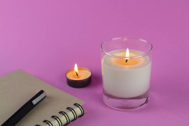 Sevgililer Günü 'nde romantik bir ortam yaratmak ve rahatlamak için sabah yatak odasında pembe mum, defter ve kalemle pembe masa üzerindeki lüks kokulu mum aromalı cam diplay.