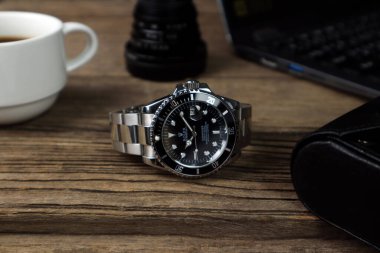 Lüks Rolex klasik kol saati seramik model siyah istiridye daimi denizaltı tarihi 40 mm ahşap masa üzerinde bir defter ve bir fincan kahveyle sabah çalışma saatinde konur.