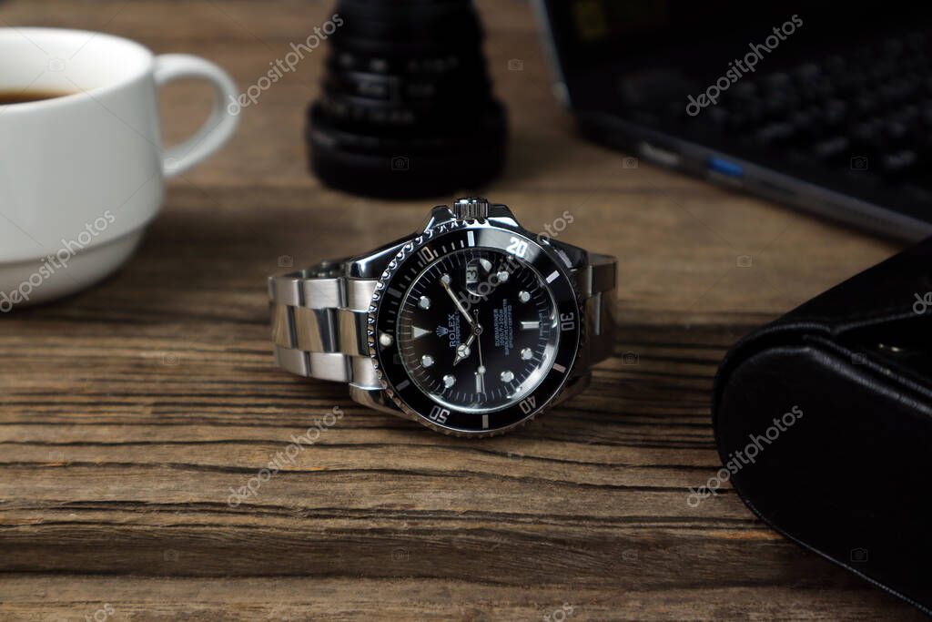 Luxurious Rolex vintage wristwatch ceramic bezel model black oyster perpetual submariner date 40 mm is put on the wooden table with a notebook and a cup of coffee in the morning while working time