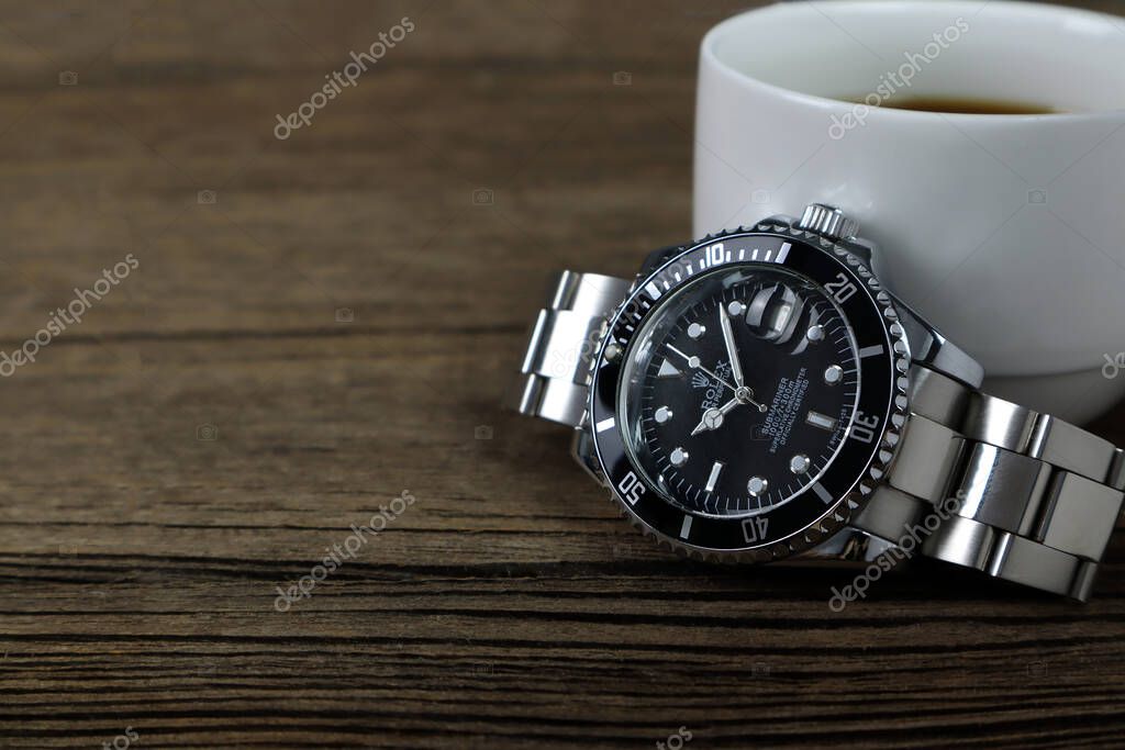 Luxurious Rolex vintage wristwatch ceramic bezel model black oyster perpetual submariner date 40 mm is put on the wooden table with a book and a cup of coffee in the morning during breakfast