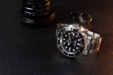 Lüks Rolex klasik kol saati seramik model siyah istiridye daimi denizaltı tarihi 40 mm siyah ahşap masa üzerinde yüzükler ve kamera lensi ile sabah çalışma saatlerinde takılır.