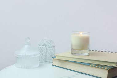 Sevgililer Günü 'nde rahatlamak ve romantik bir ortam yaratmak için yatak odasındaki beyaz beton duvarın arka planına sahip not defteriyle masada aromatik kokulu cam mum sergilenir.