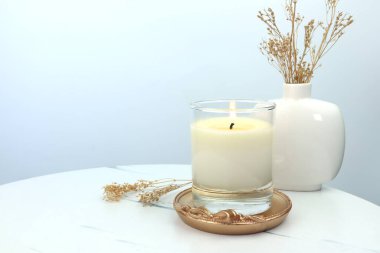 Sevgililer Günü 'nde romantik bir ortam yaratmak ve rahatlamak için beyaz çimento duvar zeminiyle beyaz masada sergilenen aromalı aromalı mum camı.
