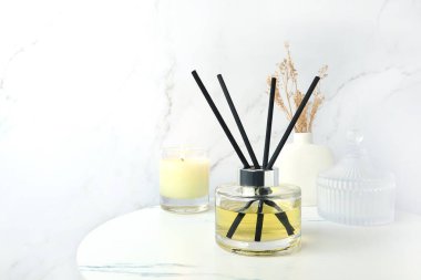 Beyaz mermer duvar arka planlı yatak odasında rahatlık ve romantik ortam yaratmak için mermer masanın üzerinde oda spreyi olarak sazlık aromalı cam şişe aroması kullanılıyor.