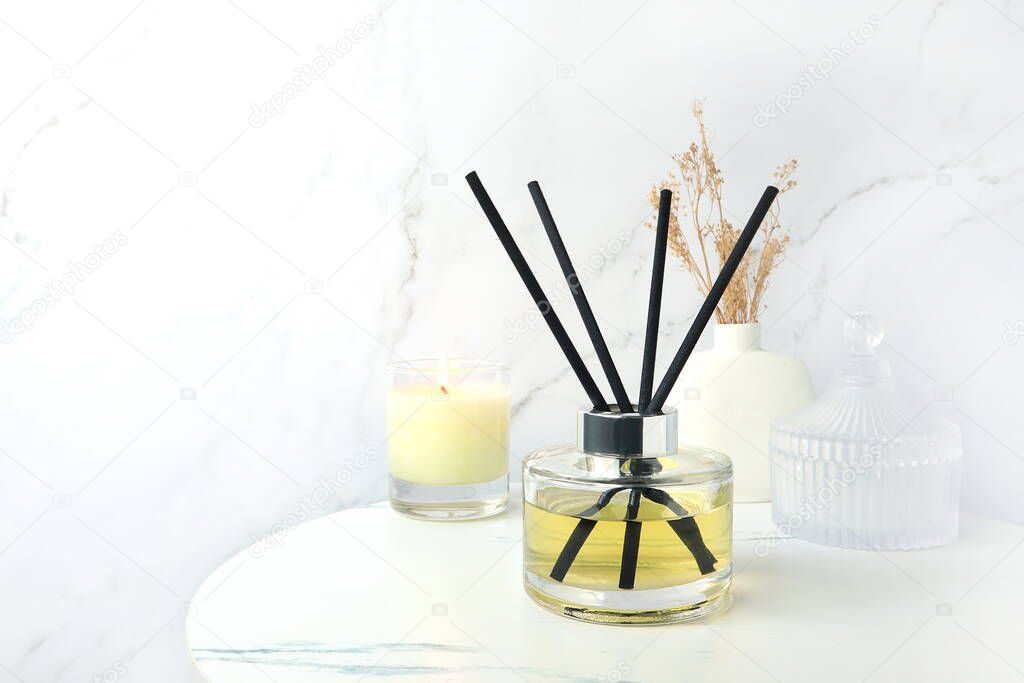 luxury aromatic scent of reed diffuser glass bottle is used as room freshener on the marble table with scented candle to create relax and romantic ambient in bedroom with white marble wall background