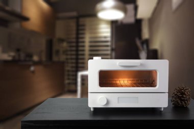 Beyaz modern tasarım tost makinesi kahverengi ahşap masanın üzerinde. Kahvaltı sırasında mutfak odasının arka planında.