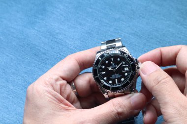 The Rolex vintage wristwatch ceramic bezel model black oyster perpetual submariner date 39 mm is in the hands being adjusted the time with background of blue table