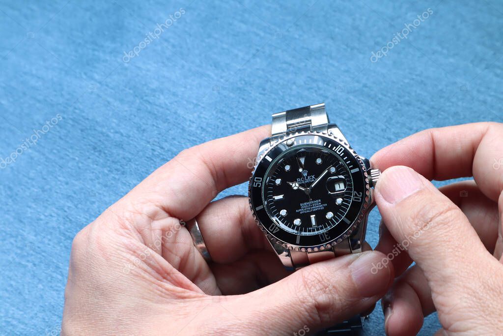 The Rolex vintage wristwatch ceramic bezel model black oyster perpetual submariner date 39 mm is in the hands being adjusted the time with background of blue table
