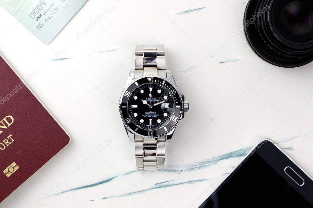 Rolex wristwatch model submariner date oyster perpetual  with black ceramic bezel stainless steel body is put on the white marble table with passport, credit card, camera lens prepared for travel