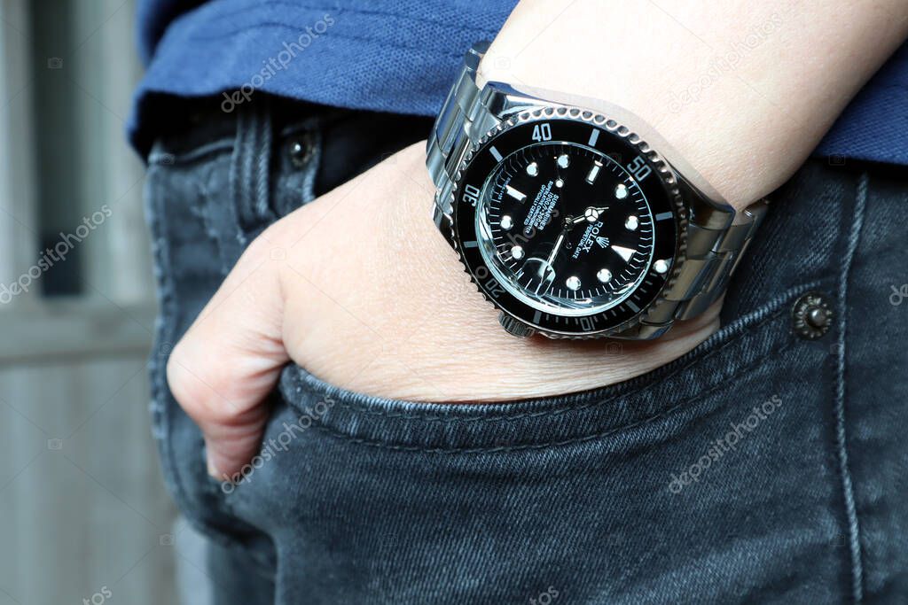 The Rolex vintage wristwatch ceramic bezel model black oyster perpetual submariner date 39 mm is on the  left hand wrist of a young man with brown wooden wall background