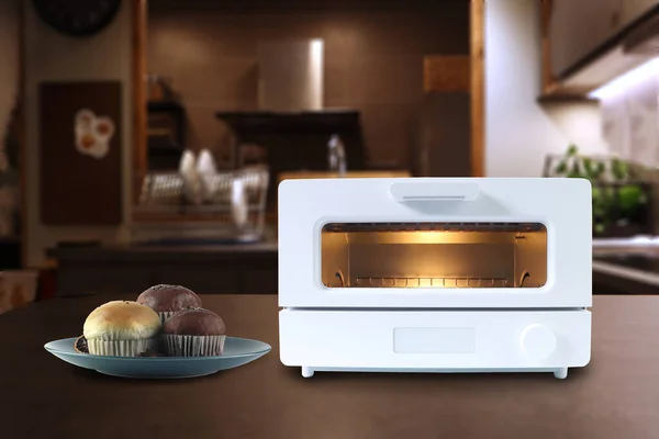 white modern design toaster oven is on the wooden table with homemade cup cake chocolate muffin on background of nice design kitchen for making breakfast in the morning