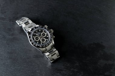 Rolex wristwatch model cosmograph daytona oyster perpetual superlative chronometer with black ceramic bezel stainless steel body display on black stone table in authorized dealer shop