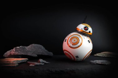 a droid robot character in the Star Wars movie name BB-8 (or Beebee-Ate) display on stone table with background of black space wall in the star war movie toy shop