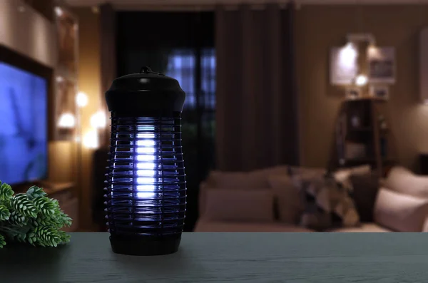 an insects mosquito electric blue light killer lamp is put on the black wooden table in the nice livingroom with background of tv and sofa to protect the mosquito during relax time