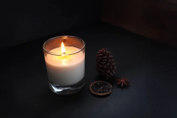 burning luxury aromatic scented candle glass on the black table with spices on background of old wooden wall of the cottage in the living room to creat relax ambient during christmas party