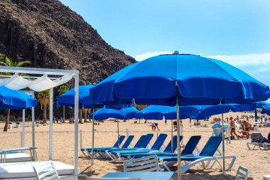 Güneşli bir günde mavi şemsiyeli ve plaj sandalyeli Las Teresitas plajı. Tenerife. Kanarya Adaları. İspanya