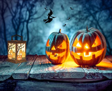 İki cadılar bayramı balkabağı ve içinde ışık olan bir masa ve gece süpürgesinde uçan bir cadı.