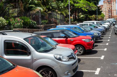 Arka planda bitkiler ve binalar olan şehir dışı araba parkı.