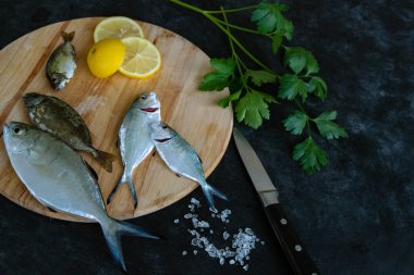 Çiğ taze balık, limon dilimleri ve tahta bir tahtanın üzerinde maydanoz. Esmer bir geçmişi var. Mutfakta balık pişiriyorum. Akdeniz 'de balık tutmak. Seçici odak.