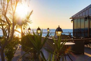 Açık hava restoranına fenerlerle bakmak ve palmiye ağacının içinden güneşi geçirmek, insan yok. Arka planda gün batımı. Seçici odak