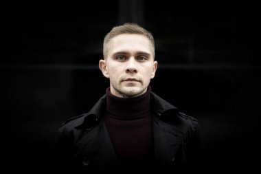 Ukrainian man in black trenchcoat and purple polo neck on black background