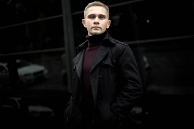 Ukrainian man in black trenchcoat and purple polo neck on black background