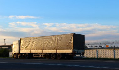 Long truck on a highway near the fence of the transport airport with planes