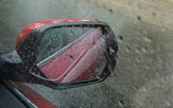 A rain drenched car side window makes it difficult to see in the rearview mirror