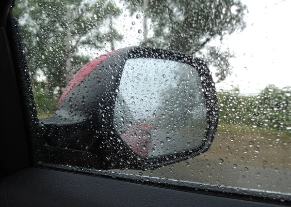 Raindrops on a side mirror and car window in heavy rain