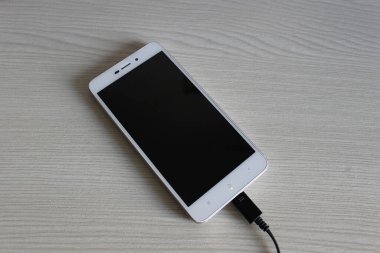 Veri transferi ve üst görünümü şarj etmek için kabloyla bağlı ahşap bir rafta ekranı kapalı cep telefonu