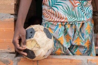 Nio afro pobre sostiene balon de futbol desinflado on muy mal estado