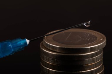 İğnenin ucunda bir damla sıvı şırınga ve 1 avroluk madeni para.