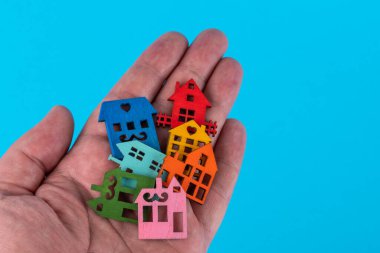 Birçok ahşap sembolik ev mavi arka planda bir erkek avucunda yatar.