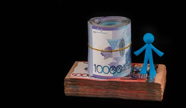 Figurine of a symbolic person with a lot of Kazakh banknotes (tenge) on a black background