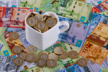 Kazak parasıyla dolu beyaz bir kupa. Kazak banknotlarının arka planına karşı 100 onluk banknot şeklinde bir kalp sembolü şeklinde.